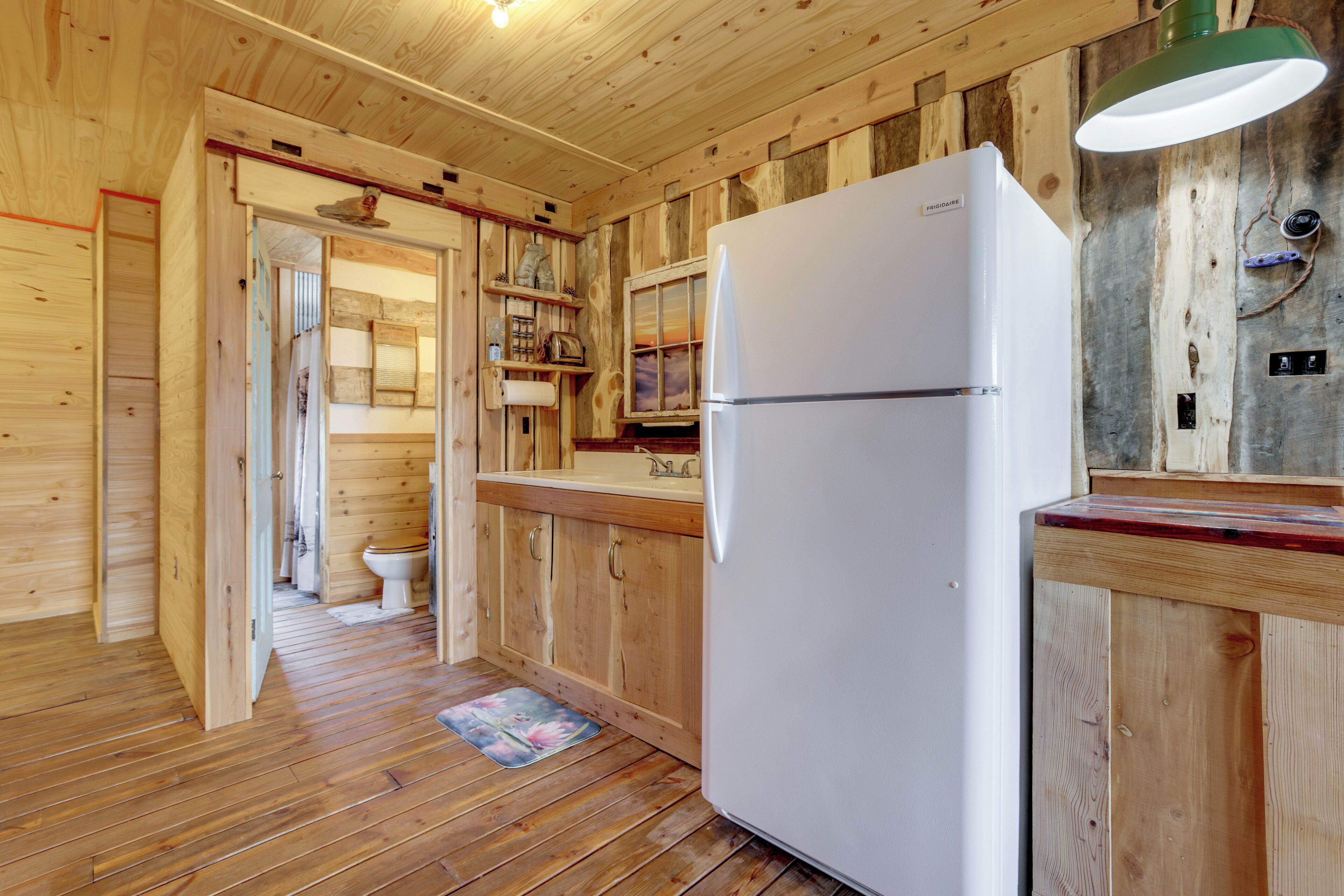 A wooden cabin interior with a kitchen area, including a refrigerator, wooden cabinets, and a wooden floor.