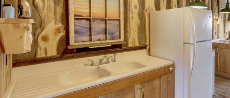 A wooden interior with a white sink, a window with a sunset view, and a white refrigerator.