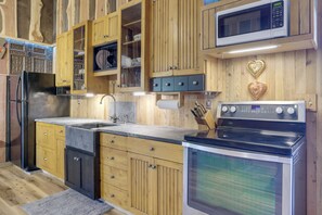 Une cuisine avec des meubles de rangement en bois, un four à micro-ondes, un four traditionnel et un évier.