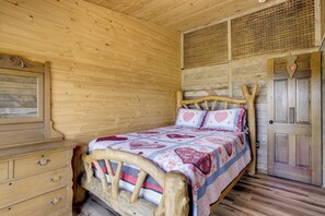 Une chambre dans une cabane en bois, avec un lit, une commode et une porte.