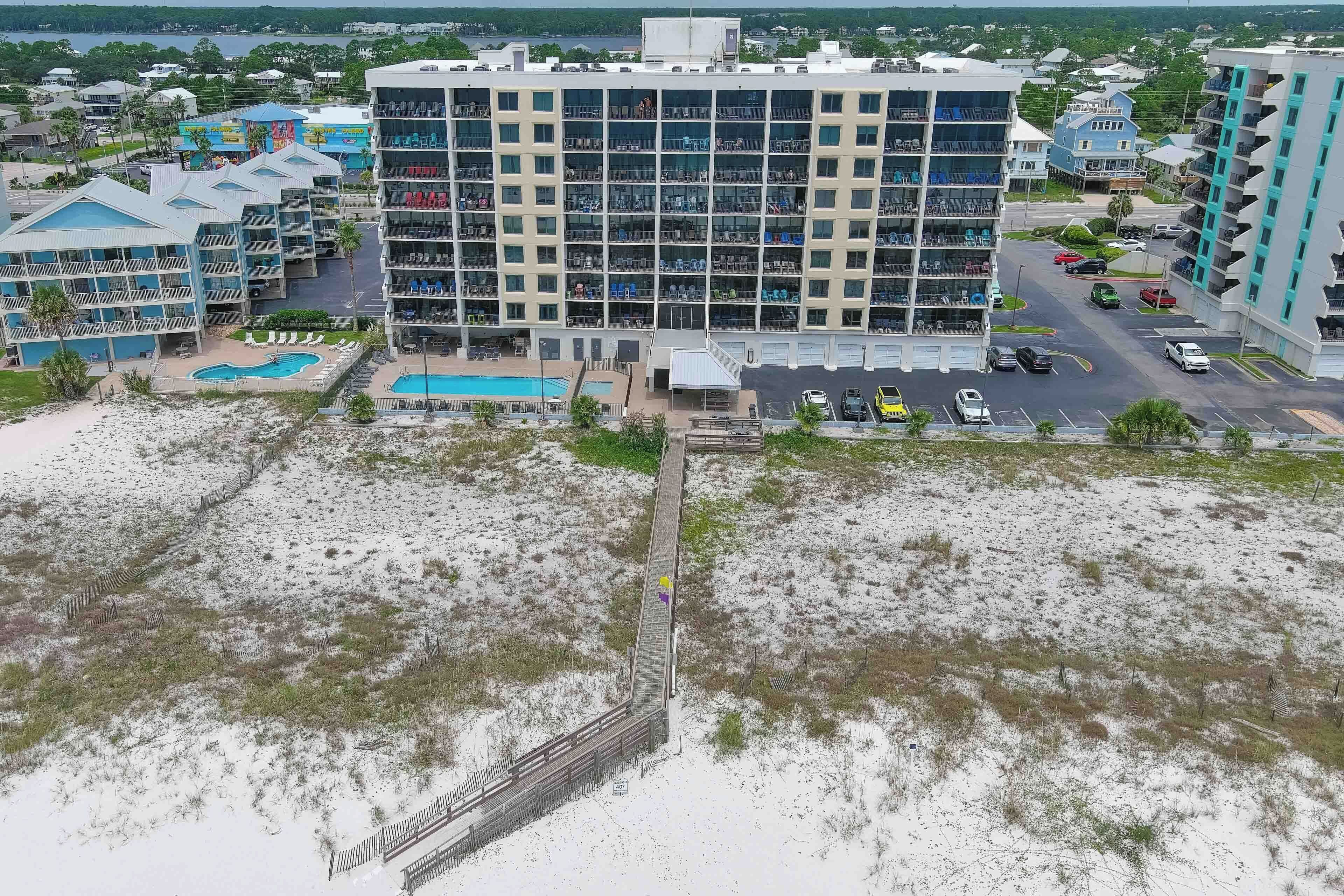 A multi-story hotel with a swimming pool, parking area, and a beach view.