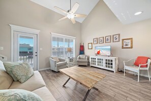 A living room with a ceiling fan, a television, a white cabinet, and a sofa with decorative pillows. - Coastal Cottage Near Beach w/ Large Decks & Backyard | BEACHBALL PROPERTIES (Gulf Shores)