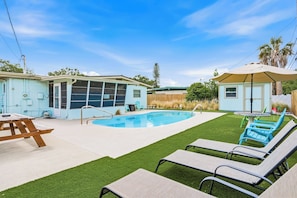 Ein Garten mit Schwimmbad, Terrassentisch und Liegestühlen.