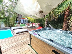Eine Holzterrasse mit Whirlpool, Schwimmbad und Gartenmöbeln.