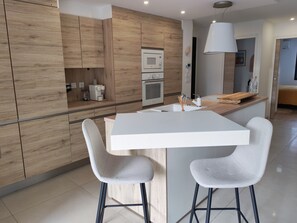 Eine moderne Küche mit Holzschränken, einer weißen Arbeitsplatte und zwei Barhocker.