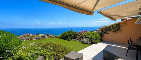 A patio with wicker furniture, a table, and a view of the ocean.