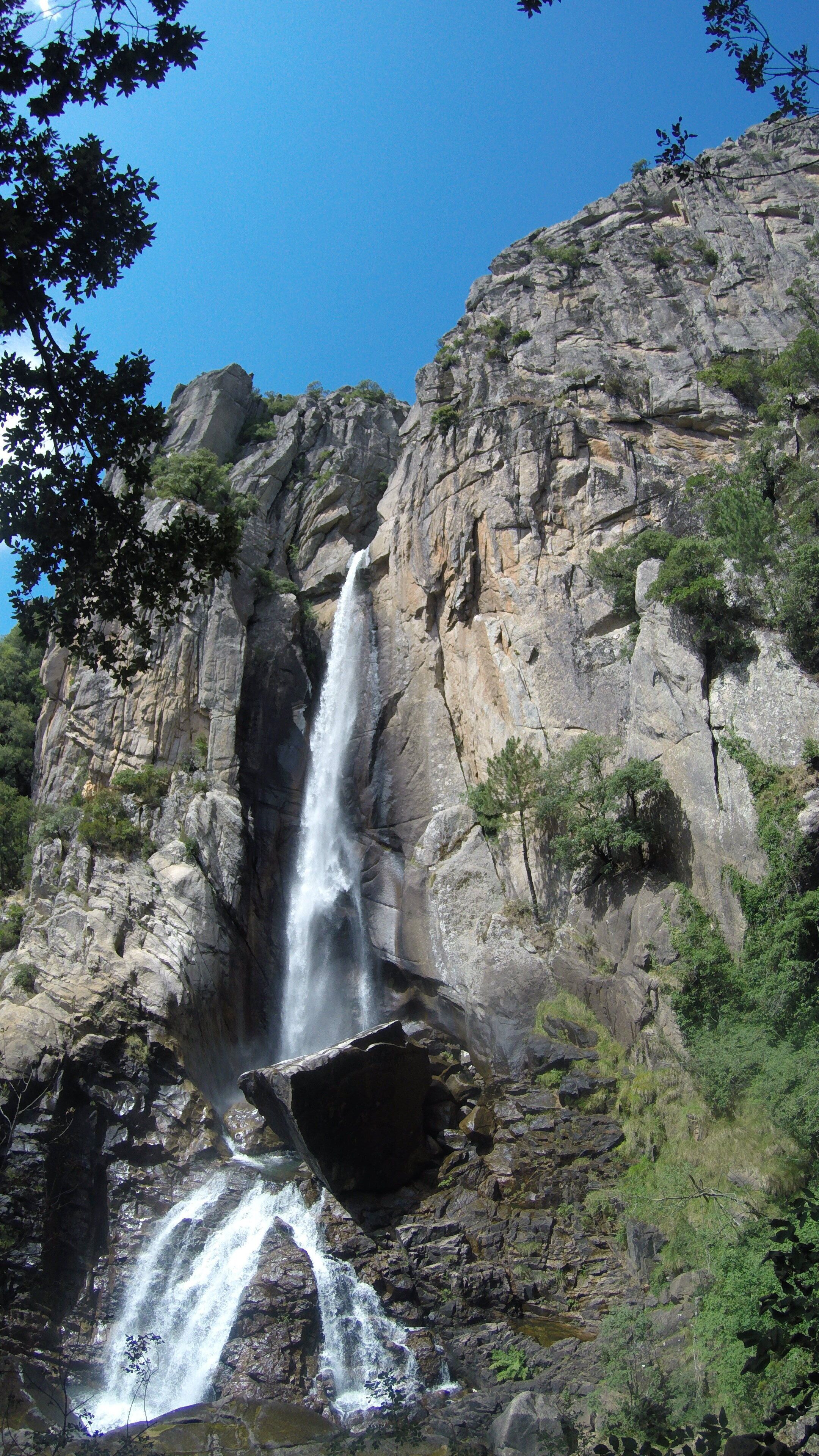 A waterfall cascading down a rocky cliff surrounded by greenery.