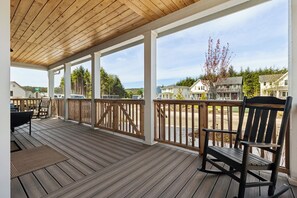 Eine überdachte Veranda mit Holzboden, einem Schaukelstuhl und Blick auf Häuser und Bäume.