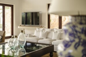 A living room with a white sofa, a glass coffee table, and a flat-screen TV mounted on the wall. - La Vida Dulce in Punta de Mita (Punta de Mita)