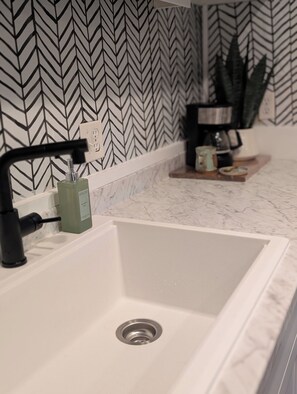 Une salle de bain avec un lavabo blanc, un robinet noir et un miroir au-dessus.