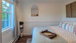 Ein Schlafzimmer mit einem großen Bett, einem kleinen Tisch mit Tablett, einer Topfpflanze und einem Spiegel an der Wand.