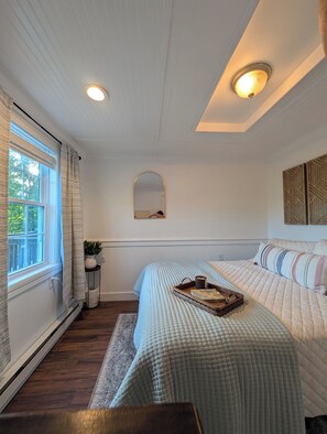 A bedroom with a large bed, a small table with a tray, a potted plant, and a mirror on the wall. - Thoughtfully design retreat created for rest, renewal, and meaningful connection (Banner Elk)