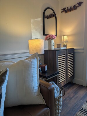 A living room with a brown leather sofa, a white cushion, a small table with a lamp, a vase with flowers, and a wooden shelf with bird decorations. - Thoughtfully design retreat created for rest, renewal, and meaningful connection (Banner Elk)