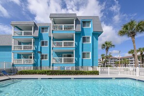 A multi-story hotel with balconies, a swimming pool, and palm trees.