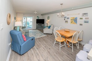 A living room with a sofa, a TV, a dining table with chairs, and a balcony.
