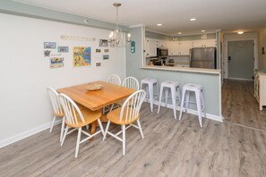 A kitchen with white cabinets, a stainless steel refrigerator, and a wooden dining table with white chairs.