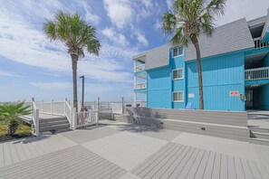 A blue building with balconies, a wooden deck, and palm trees.