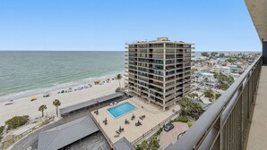 A high-rise hotel with a pool, beach view, and a cityscape in the background. - 🌞Sunsets, Gulf and Beach Views🐬Great Amenities🌴Mansions By The Sea 1103A (Treasure Island)