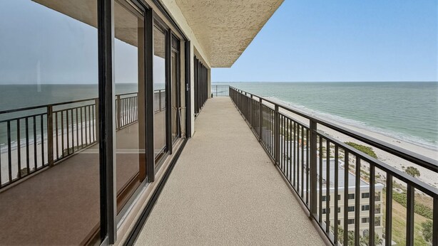 A balcony with a view of the ocean, a covered walkway, and a building in the background. - 🌞Sunsets, Gulf and Beach Views🐬Great Amenities🌴Mansions By The Sea 1103A (Treasure Island)