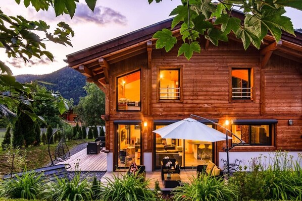 Eine Holzhütte mit einer Terrasse, Sitzgelegenheiten im Freien und einem großen Sonnenschirm.