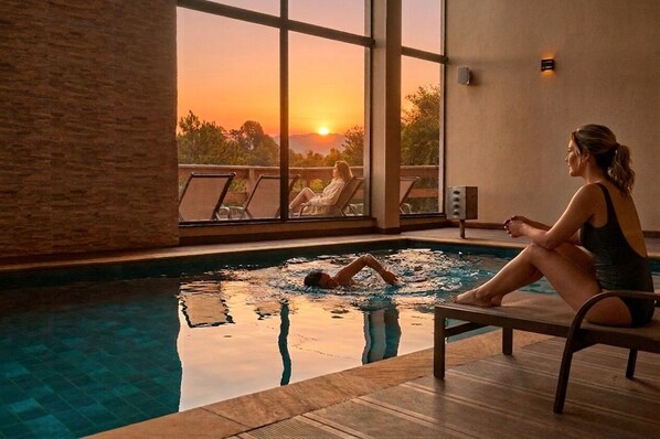 A swimming pool with a sunset view, lounge chairs, and a person sitting by the pool.
