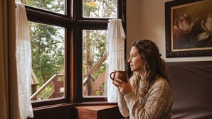A person sitting by a window with curtains, holding a mug. - Pousada Recanto dos Sonhos (Campos do Jordão)