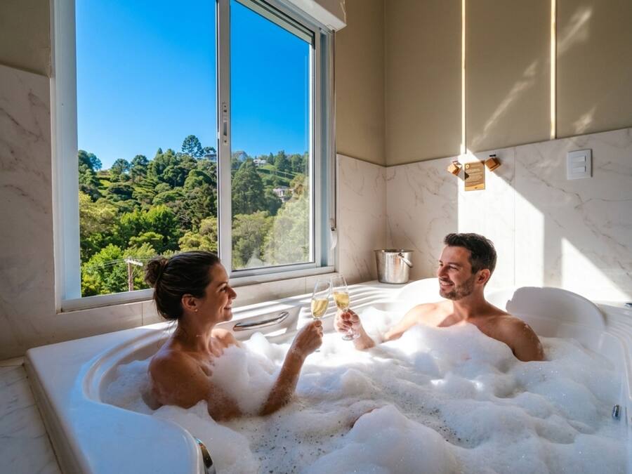 A room with a large window, a bathtub filled with bubbles, and a view of greenery outside.