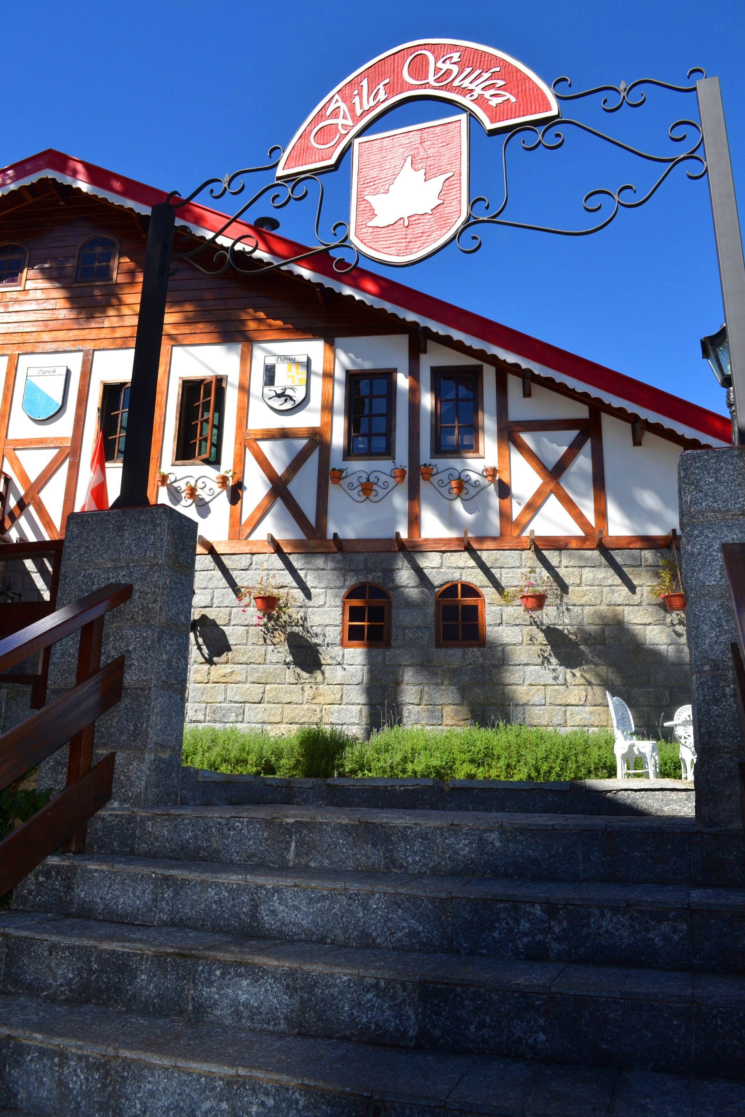 Um edifício tradicional com fachada vermelha e branca, uma placa acima da entrada e degraus de pedra que levam à porta.