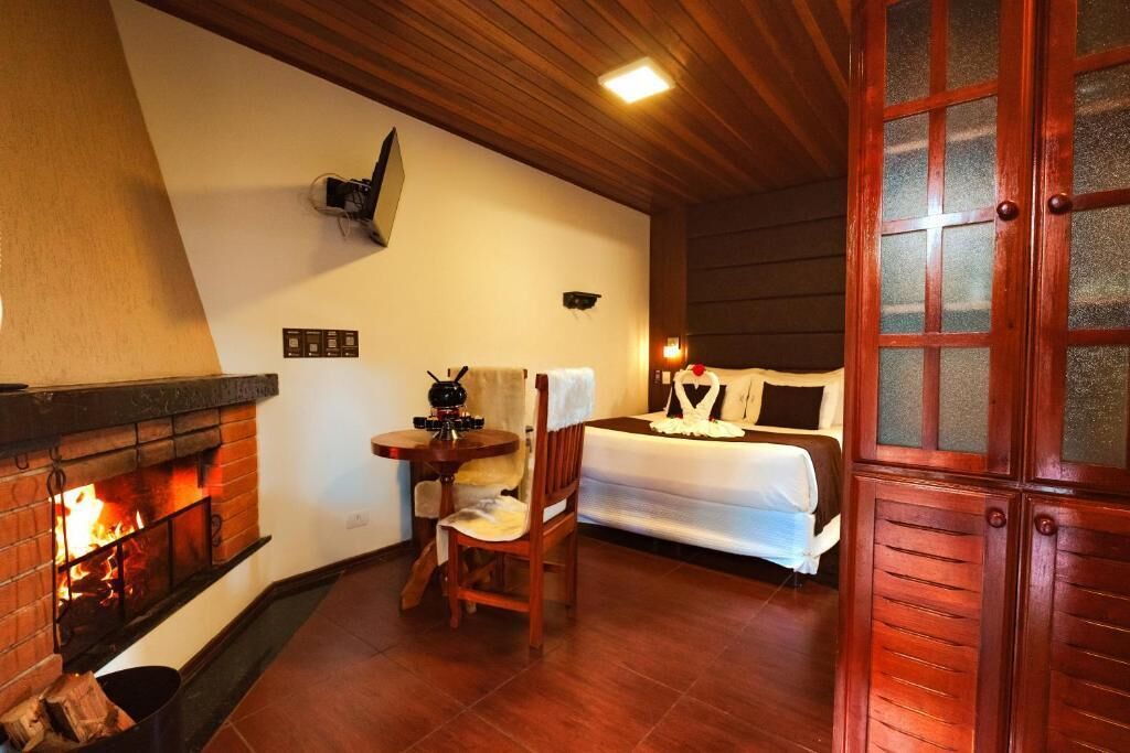Una habitación con chimenea, una cama, una mesita con una silla y una puerta de madera.