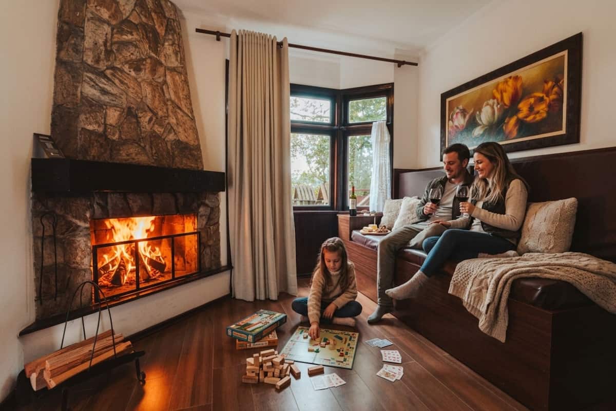 A cozy living room with a fireplace, a couch, a child playing with wooden blocks, and a couple sitting on the couch.