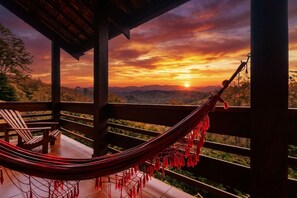 Una hamaca en una terraza de madera con vistas a un paisaje montañoso al atardecer.