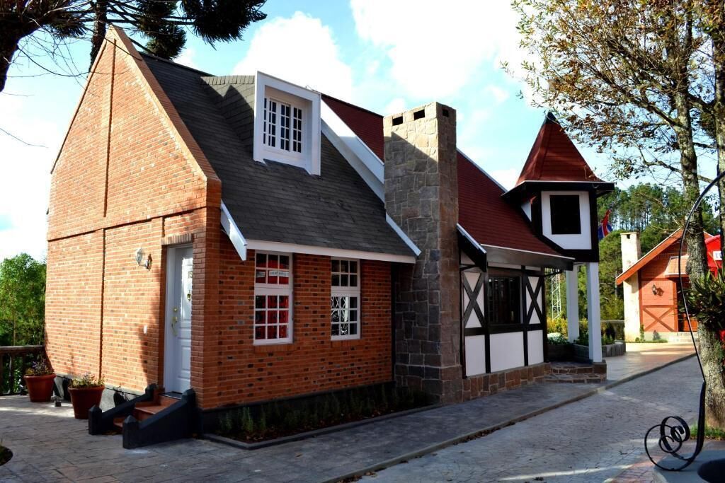 A traditional brick building with a steeply pitched roof, a stone chimney, and a small window with a grid pattern.