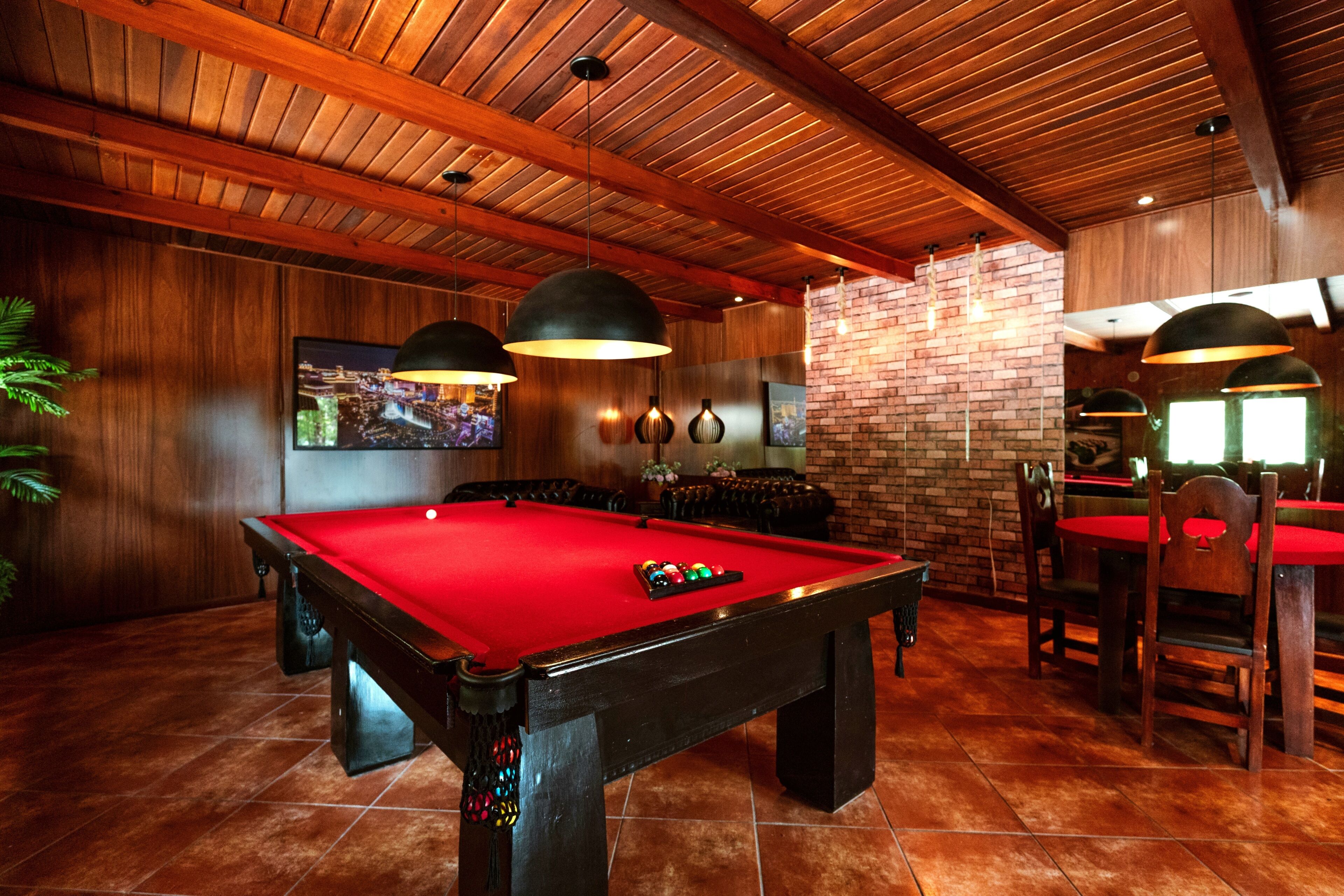 Uma mesa de bilhar com bolas, cercada por paredes de madeira e uma parede de tijolos decorativa.