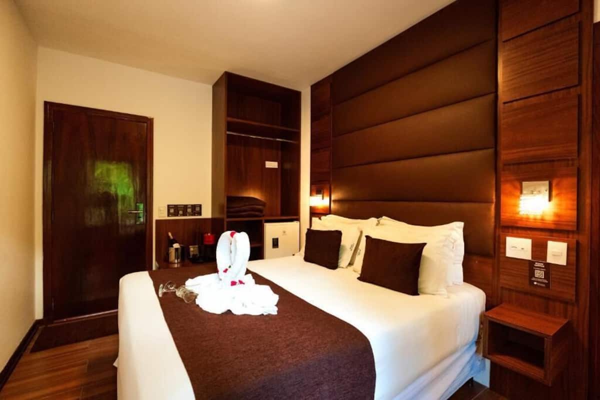 A hotel room with a large bed, wooden headboard, bedside tables, and a wardrobe.