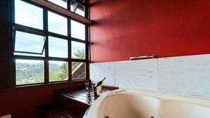 A bathroom with a large bathtub, a window with a view, and a wooden bench. - Pousada Recanto dos Sonhos (Campos do Jordão)