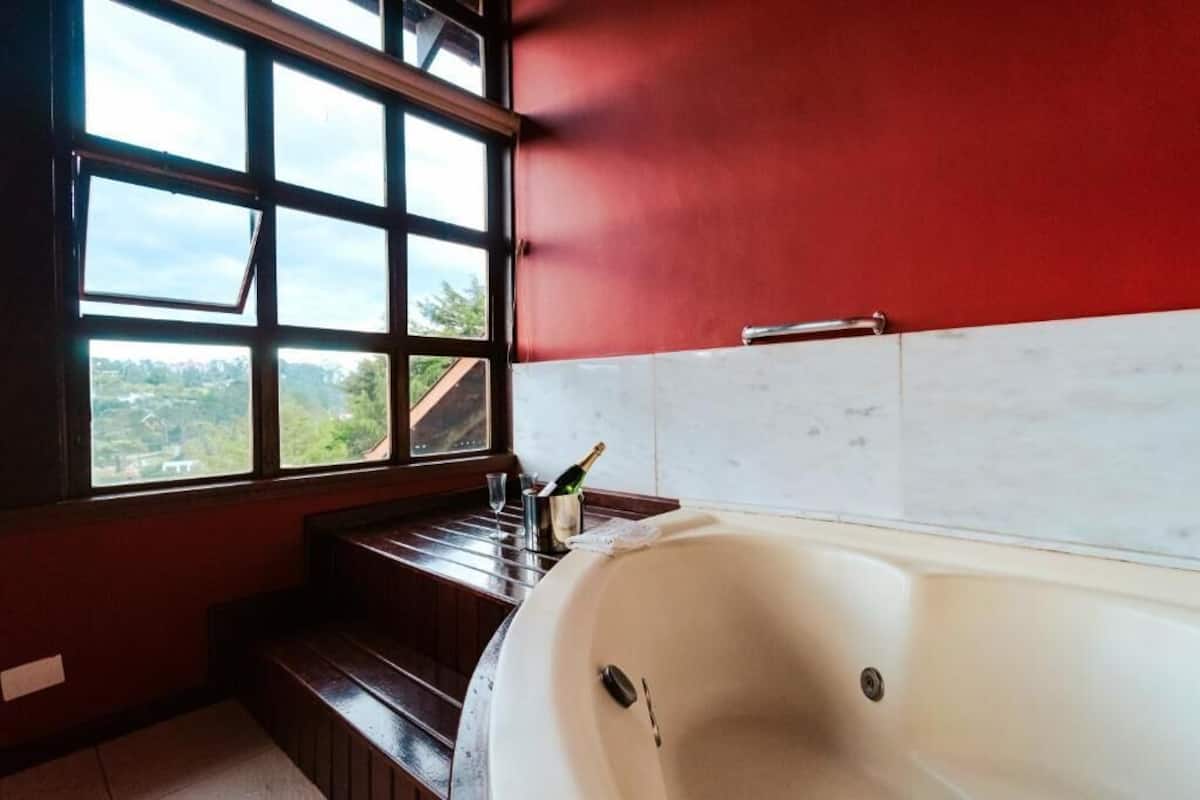 A bathroom with a large bathtub, a window with a view, and a wooden bench.
