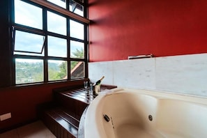 A bathroom with a large bathtub, a window with a view, and a wooden bench. - Pousada Recanto dos Sonhos (Campos do Jordão)