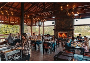 A restaurant with wooden beams, large windows, and a fireplace.
