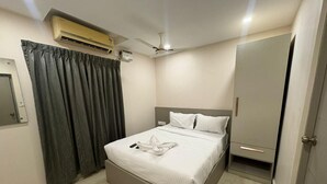 A bedroom with a bed, an air conditioning unit, a ceiling fan, a wardrobe, and a door. - Hotel Royal King (Chennai)