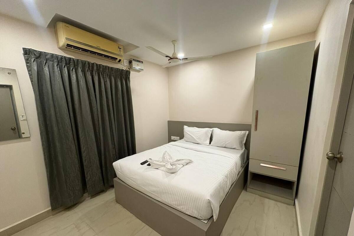 A bedroom with a bed, an air conditioning unit, a ceiling fan, a wardrobe, and a door.