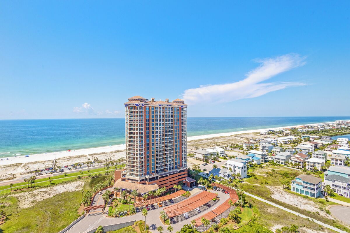 A high-rise hotel with a beach view, parking area, and a pool.