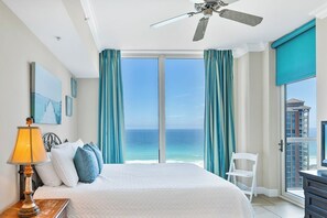 Ein Hotelzimmer mit Bett, Deckenventilator, Blick auf den Ozean und Balkon mit Stadtblick.