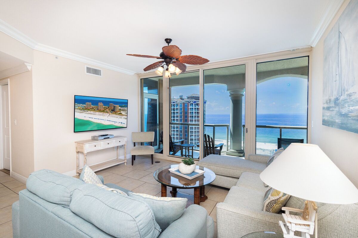 A living room with a TV, sofa, coffee table, and a balcony with a view of the sea.