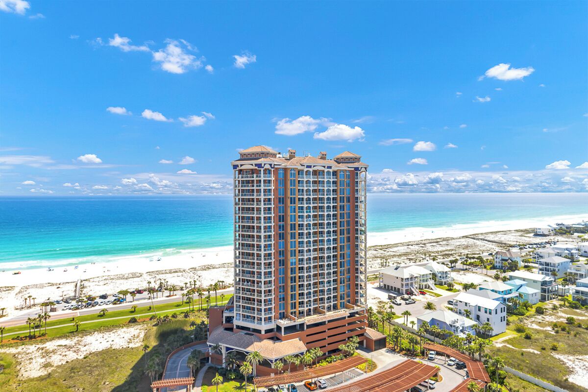 A high-rise hotel with a beach view, multiple balconies, and a parking area.