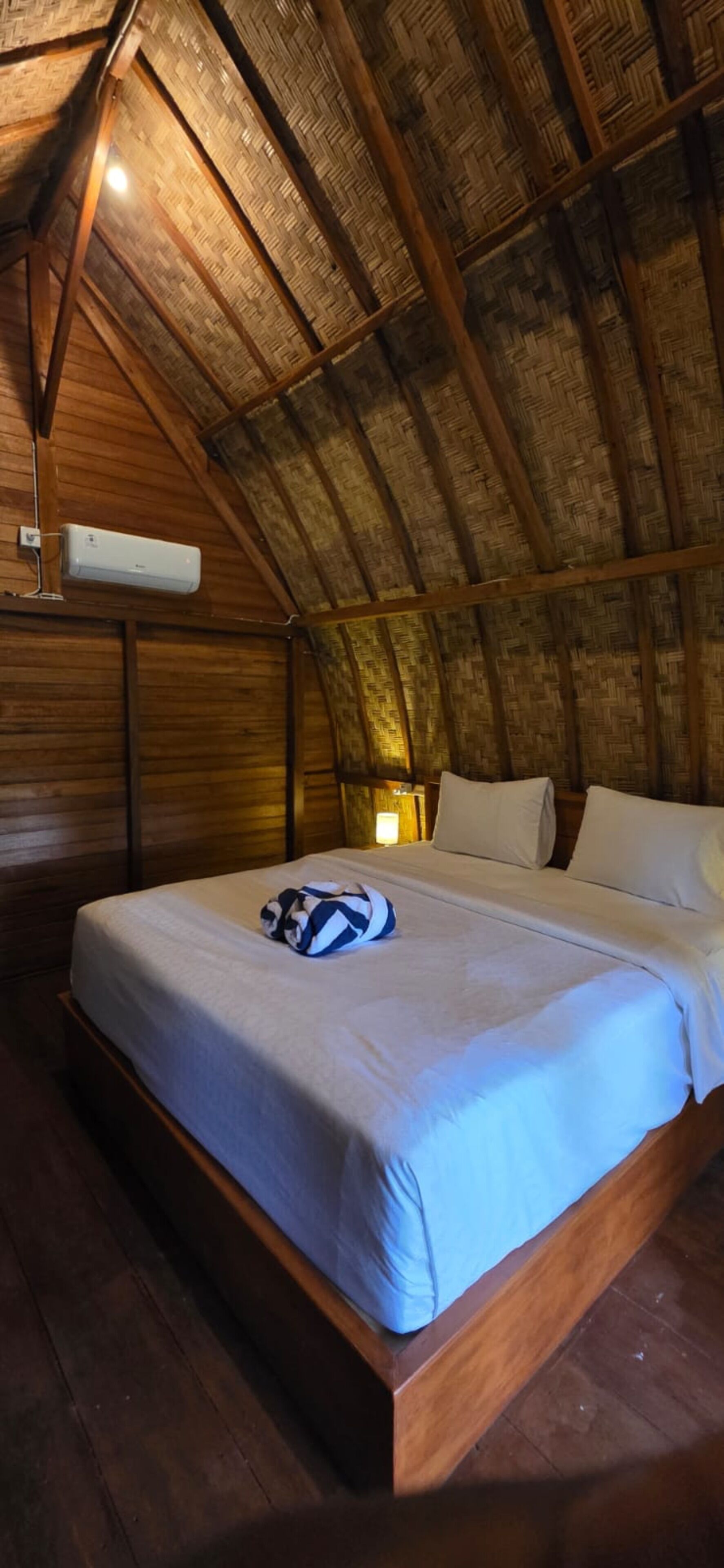 Uma cama de solteiro num quarto com teto inclinado e vigas de madeira.
