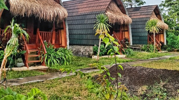 Una hilera de cabañas con techos de paja, barandillas de madera y un jardín con césped.