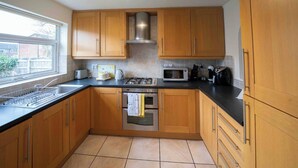 A kitchen with wooden cabinets, a gas stove, a microwave, and a sink. - 3-bed Westhoughton, Contractors and Parking (Bolton)
