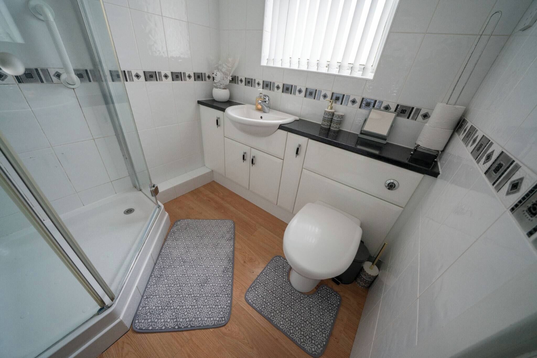 Une salle de bain équipée d’une douche, de toilettes, d’un lavabo et d’une fenêtre avec des stores.
