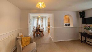 A room with a dining area, a TV mounted on the wall, and a chair with a cushion. - 3-bed Westhoughton, Contractors and Parking (Bolton)