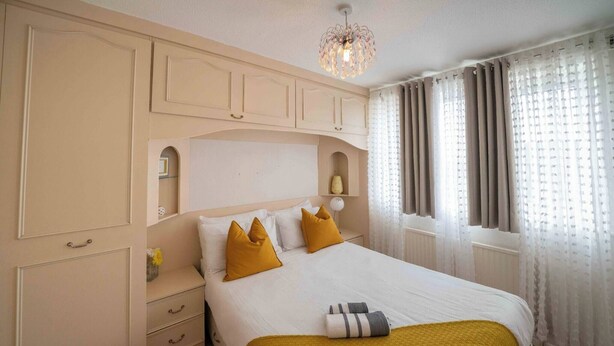 A neatly arranged hotel room with a bed, a nightstand, a dresser, and a window with curtains. - 3-bed Westhoughton, Contractors and Parking (Bolton)
